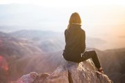 Una joven mira la luz del sol desde lo alto de una montaña.