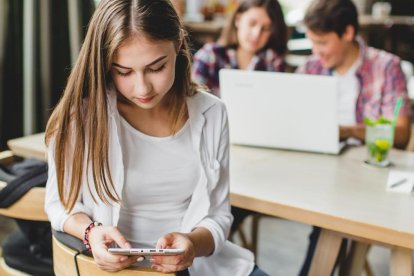 Una chica usando el móvil con sus compañeros de clase.