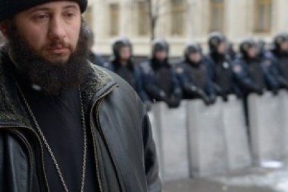 Un cura -no sabemos si católico bizantino u ortodoxo- reza en silencio mientras se pasea interponiéndose entre manifestantes y policías