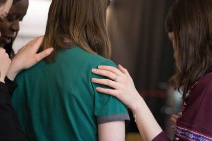 Unas mujeres oran intercediendo por otra con el gesto de imponer las manos