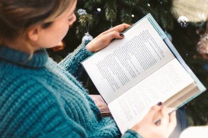 Una mujer lee un libro entre adornos navideños, foto de Red Charlie en Unsplash