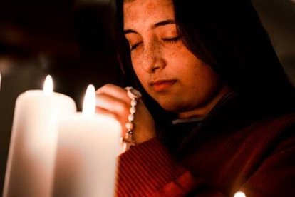 Una joven reza el rosario entre velas