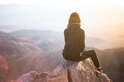 Una joven mira la luz del sol desde lo alto de una montaña.