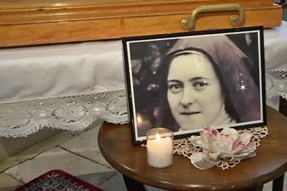 Una vela y un retrato de Santa Teresita, junto al arca que contiene sus reliquias.