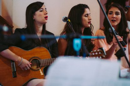 Chicas jóvenes cantando en una iglesia con una guitarra.