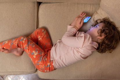 Niña con movil echada en un sofá