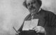 G.K.Chesterton sostiene una pluma y un libro en una foto de posado