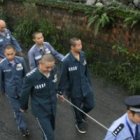 Un policía conduce numerosos presos de un campo de trabajo chino tomados de una cuerda