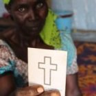 Godiya Ousman con su tarjeta-cartilla de bautismo - ha huido de Nigeria para salvar su vida y mantener su fe