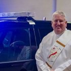 El diácono Rhein junto a un coche de la policía local- foto de  Matthew Rich para Detroit Catholic