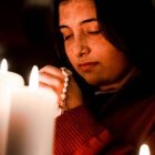 Una joven reza con velas y el rosario, foto de Gianna B para Unsplash