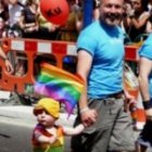Una pareja homosexual lleva a un niño pequeño con emblemas LGBT a la Marcha del Orgullo Gay