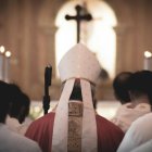 Un obispo rodeado de sacerdotes, vistos de espaldas en una iglesia.