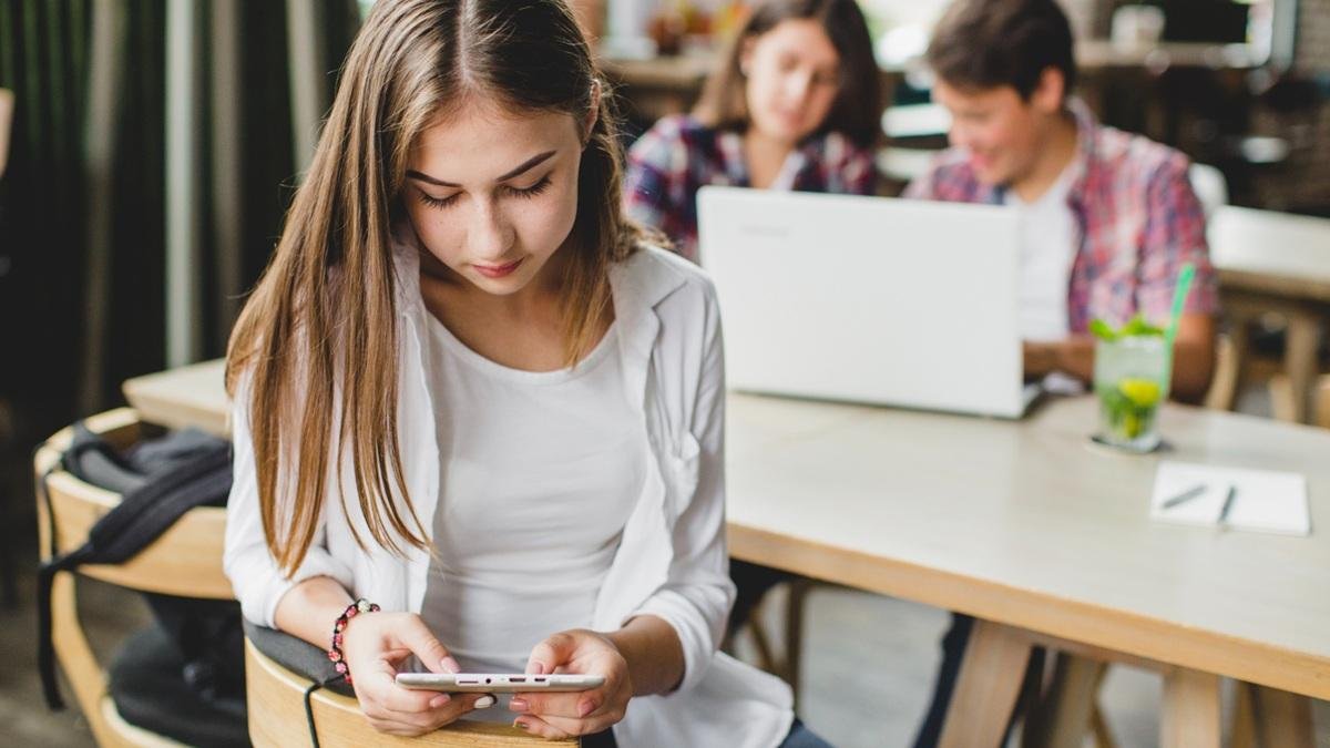 Una chica usando el móvil con sus compañeros de clase.