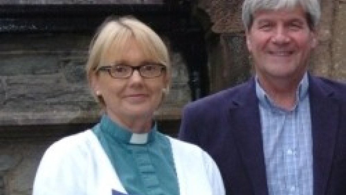 La reverenda Pat Storey con un feligrés, alzacuellos, camisa verde-irlandés y rebequita blanca