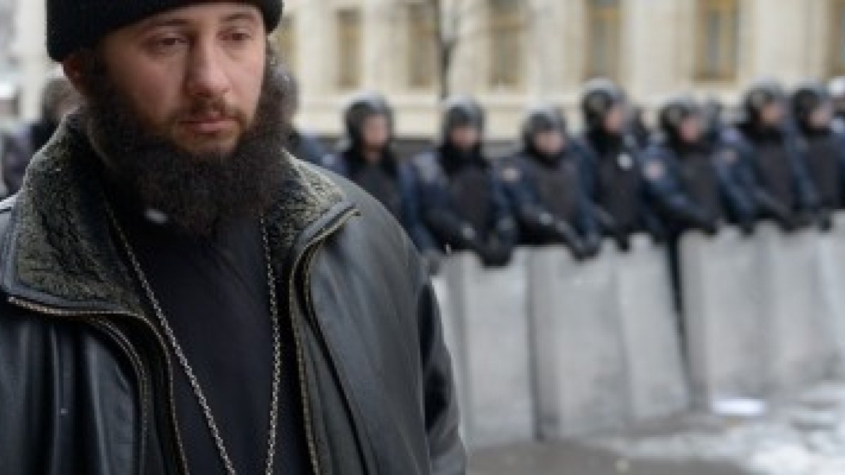 Un cura -no sabemos si católico bizantino u ortodoxo- reza en silencio mientras se pasea interponiéndose entre manifestantes y policías