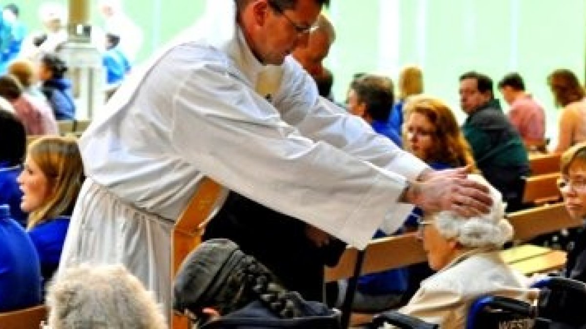 Un sacerdote ora por unas enfermas en silla de ruedas... forma parte de la misión del sacerdote abrazar su vocación sanadora