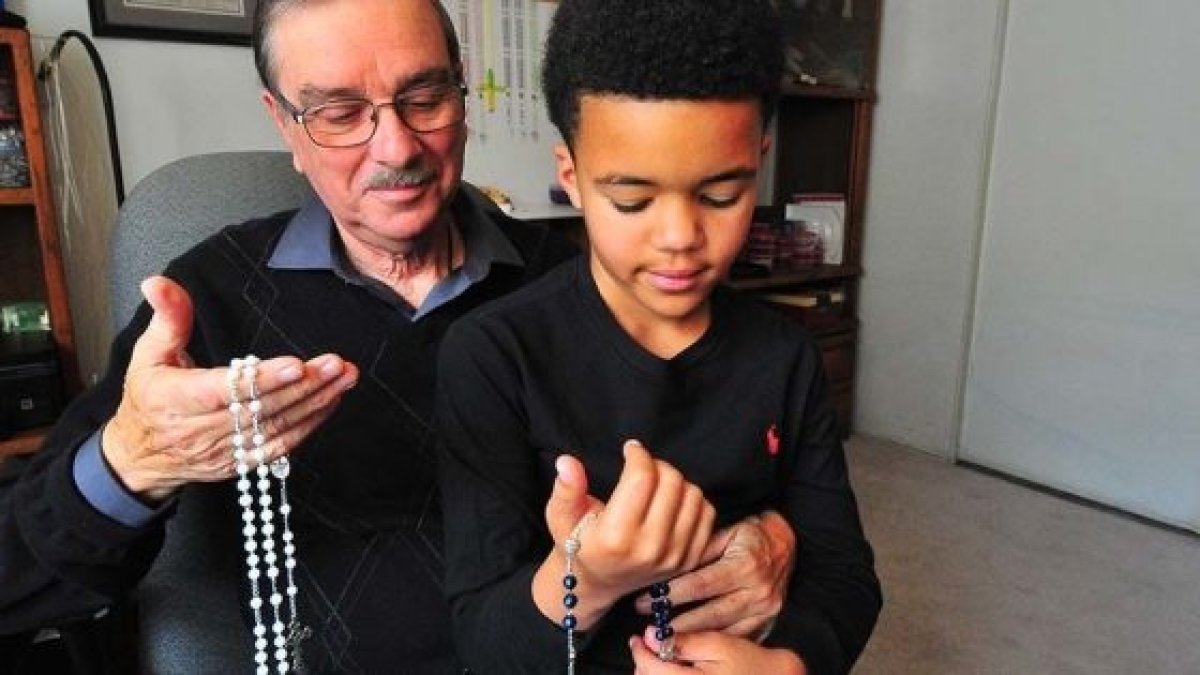 Toni Blanco con su bisnieto que le ayuda a hacer rosarios. Foto: Chris Stone. Times of San Diego.