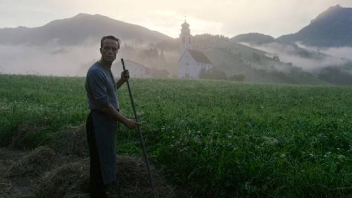 El personaje del beato Franz trabaja los campos desde la sombra... pero, más allá, el campanario y la luz apuntan al Cielo