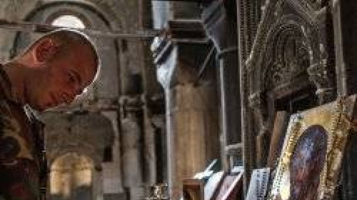 Un cristiano enciende una vela ante un icono de Cristo con rosarios y una vela de San Charbel en una iglesia destruida de Oriente