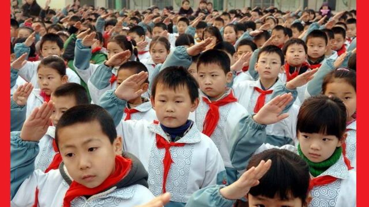 Escolares chinos en formación hacen el saludo comunista con su pañuelo rojo de pioneros comunistas