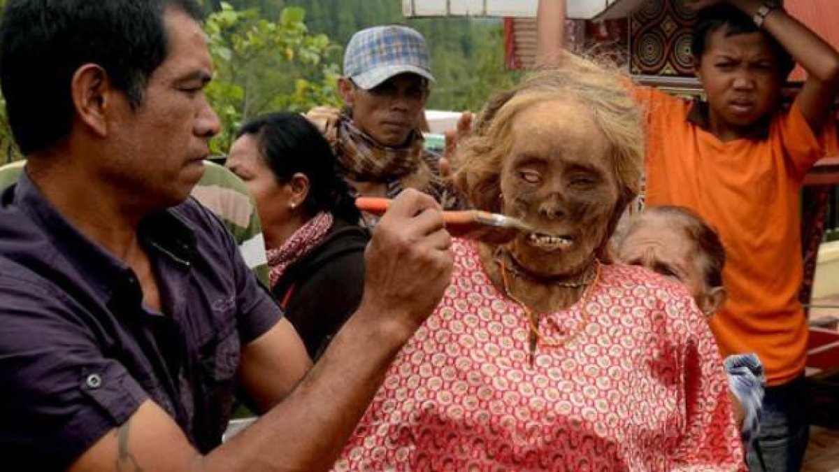 Un hombre da de comer a una pariente difunta, después de ponerle ropa nueva, en la famadihana de Madagascar