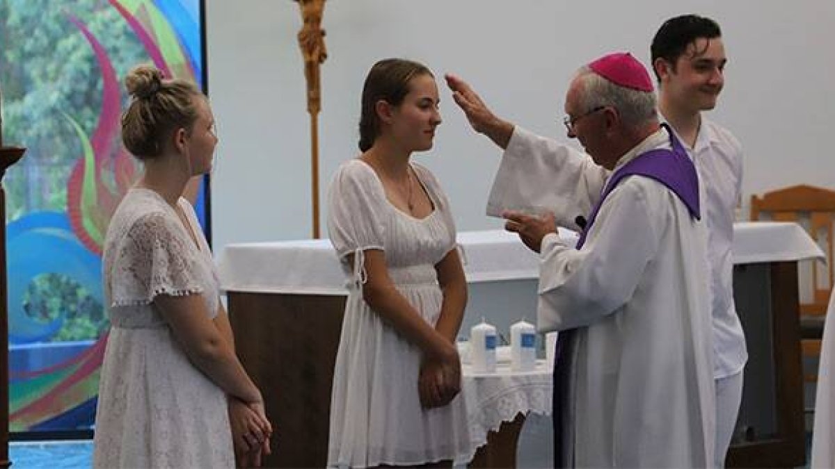 El obispo Breenan unge y confirma a 3 jóvenes revestidos con el blanco del bautismo... en el centro, Hayley, mencionada en el reportaje