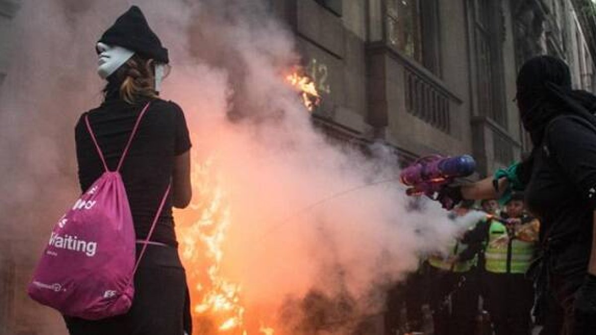 Incendio provocado en una marcha de feministas abortistas en México - unas encapuchadas echan un chorrito de agua, quizá arrepentidas
