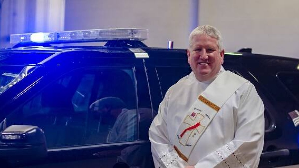 El diácono Rhein junto a un coche de la policía local- foto de  Matthew Rich para Detroit Catholic