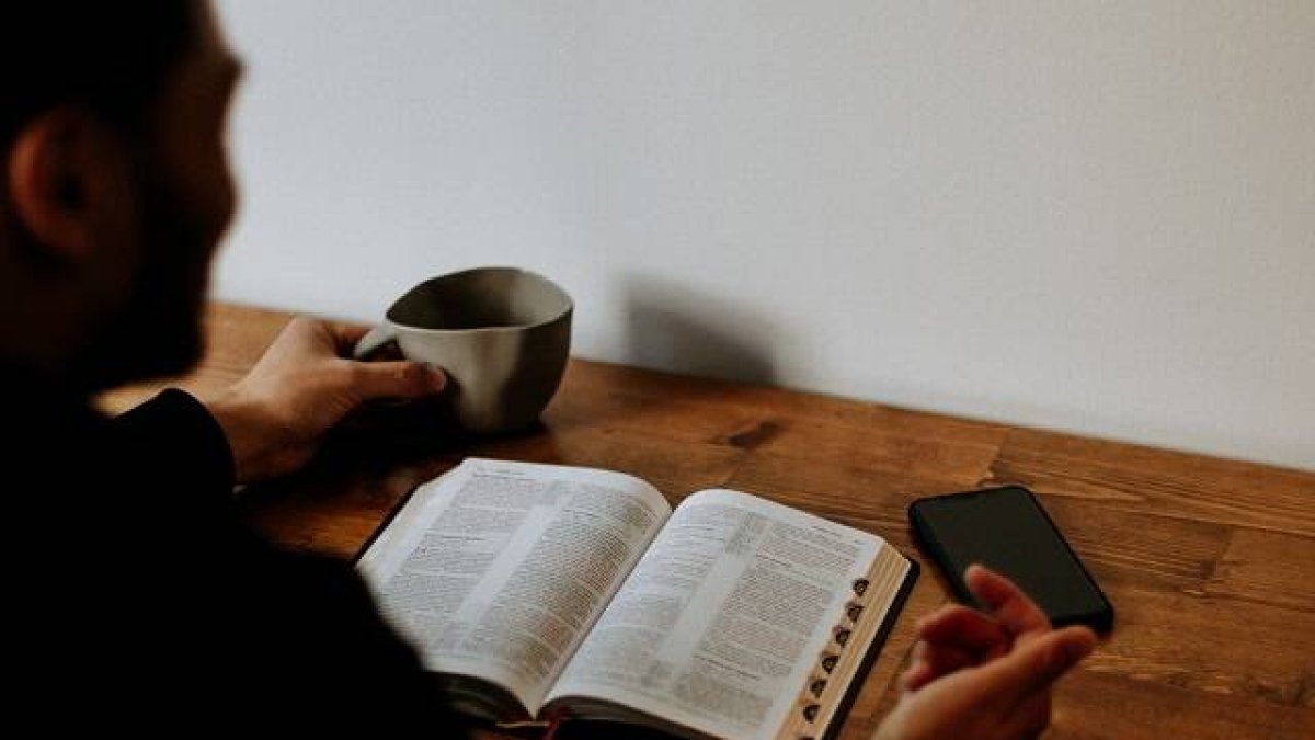 Un hombre lee la Biblia mientras toma una bebida, foto de Priscilla Du Preez en Unsplash