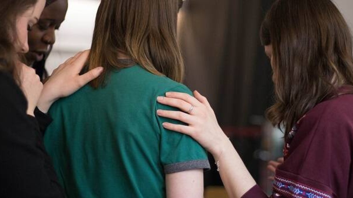 Unas mujeres oran intercediendo por otra con el gesto de imponer las manos.