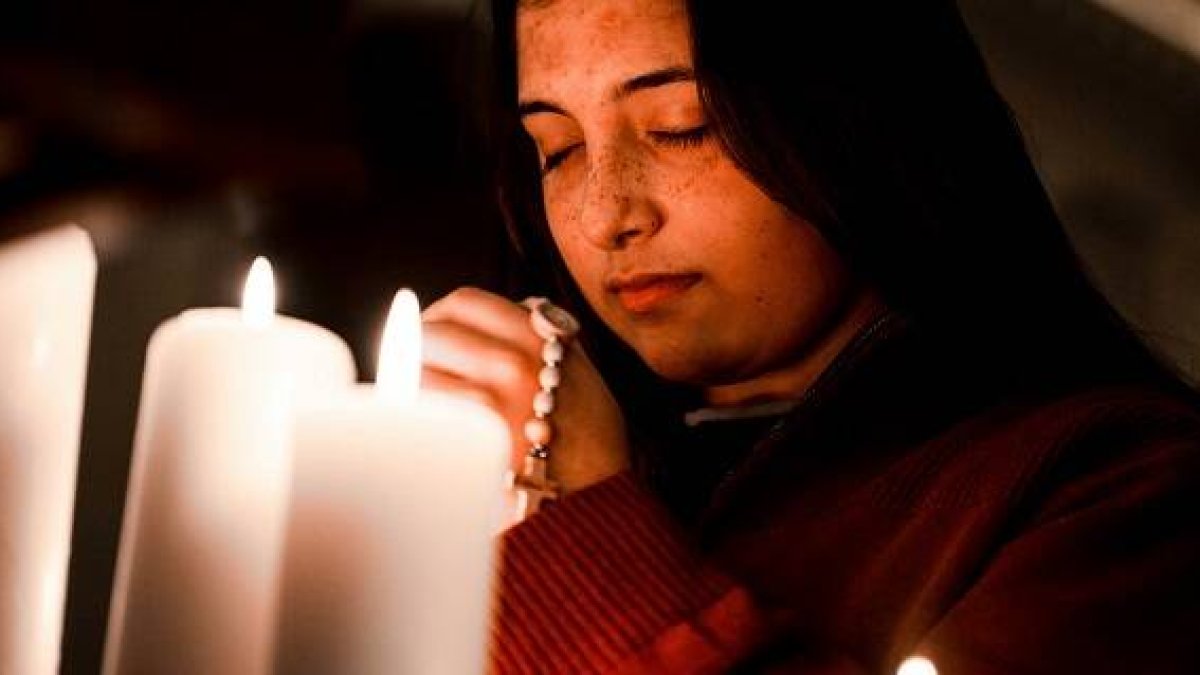 Una joven reza el rosario entre velas