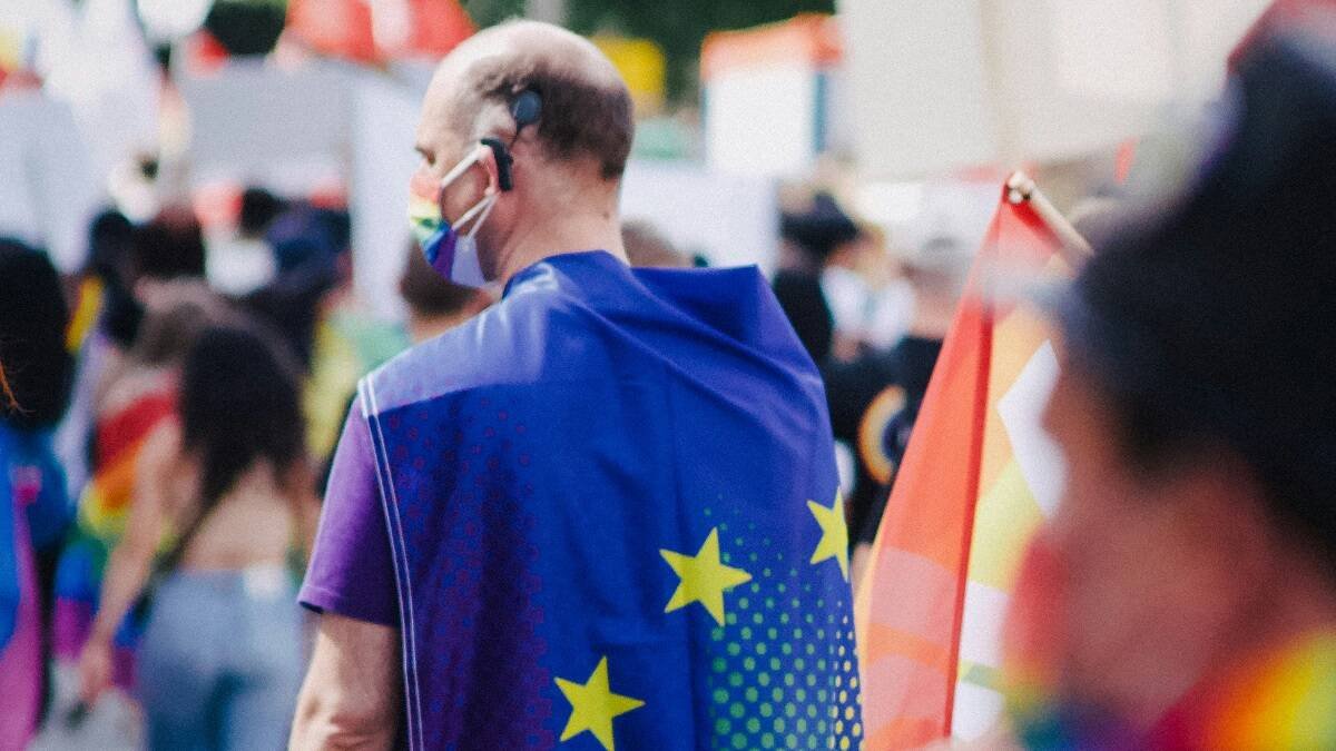 Un hombre con la bandera europea y colores arcoiris, foto de Christian Lue en Unsplash