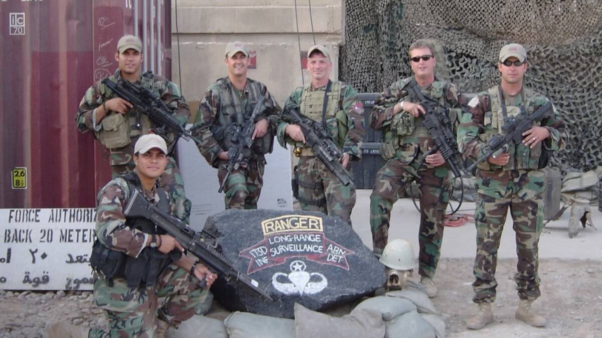 Santos, con su unidad en Irak, a la izquierda detrás del soldado arrodillado.