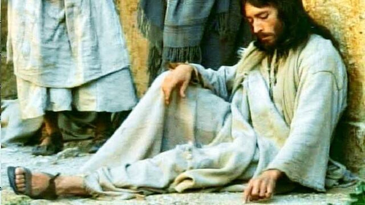 Jesús (Robert Powell) escribe tranquilamente en el suelo en la escena de la lapidación de la adúltera en 'Jesús de Nazaret' de Franco Zeffirelli (1977).