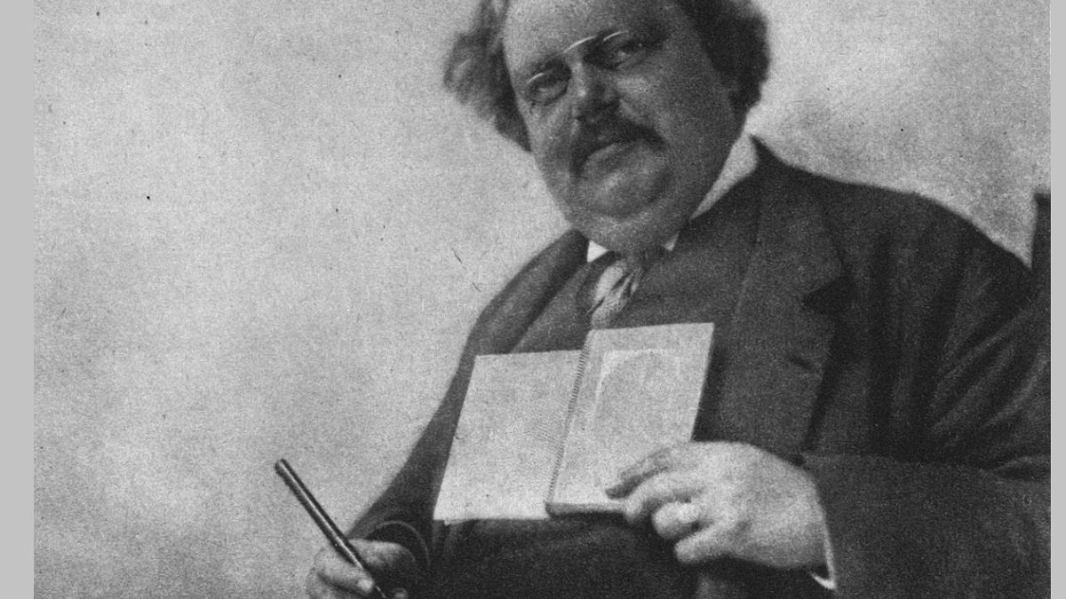 G.K.Chesterton sostiene una pluma y un libro en una foto de posado