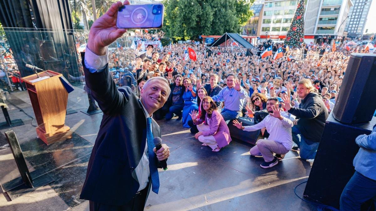 José Antonio Kast, en el cierre de uno de sus últimos mítines de campaña. En el centro de la imagen, agachada con traje de color lila, su esposa Pía.