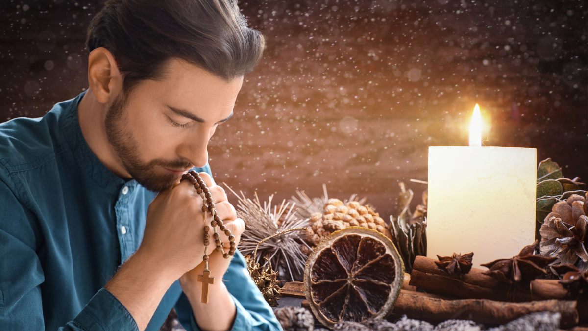 Un hombre rezando el rosario, en el marco de una corona de Adviento que prepara para la llegada de la Navidad.