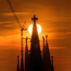 La torre de Jesucristo de la Sagrada Familia se recorta sobre el sol poniente mientras culminan las obras de la cruz.