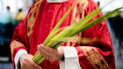 Un sacerdote revestido de rojo, con palma, en el Domingo de Ramos